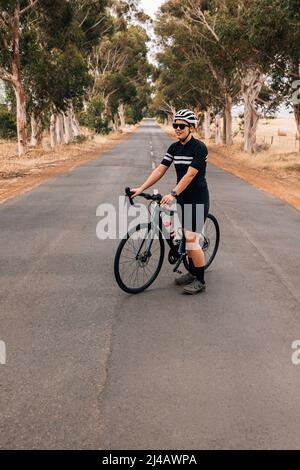 Giovane donna in abbigliamento sportivo in piedi su una strada vuota con bicicletta Foto Stock