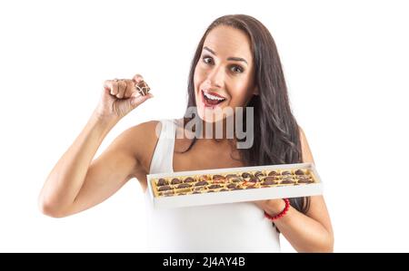 Faccia felice di un brunnete attraente che mostra che è pronto a mangiare una caramella gustosa al cioccolato da una scatola piena di caramelle. Sfondo isolato. Foto Stock