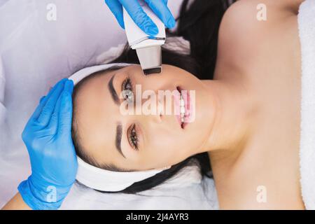 Vista dall'alto foto di una donna felice viso subisce la procedura di ringiovanimento viso con peeling ultrasonico in clinica salone di bellezza. Foto Stock