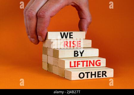 Alziamo sollevando un altro simbolo. Parole di concetto si alza sollevando altri su blocchi di legno. Mano dell'uomo d'affari. Bellissimo sfondo arancione. Il nostro business Foto Stock