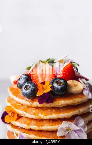 Primo piano di frutta e fiori commestibili sulla cima di una pila di pancake Foto Stock