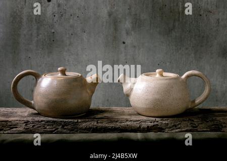 Due bollitore artigianale in teiera in ceramica fatto a mano per la cerimonia del tè in piedi su un vecchio ripiano in legno con parete grigia sullo sfondo Foto Stock