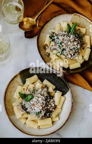 Pasta Rigatoni, con panna, funghi, spinaci, mandorle e parmigiano grattugiato, in piatti fatti a mano, e bicchiere di vino bianco, tovaglia di lino ocra, g Foto Stock