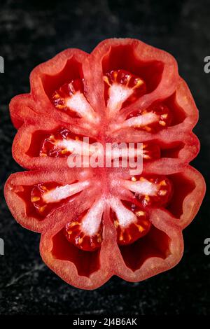 Mezzo pomodoro a cuore di manzo, posto su un piatto nero, su un piatto nero testurizzato, vista dall'alto Foto Stock
