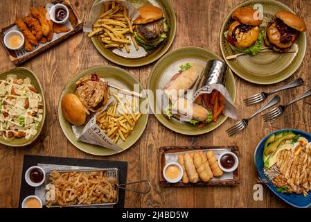 Set di piatti fast food con hamburger assortiti, sandwich, patatine fritte, tequeños, strisce di pollo fritte e caesar Salad Foto Stock