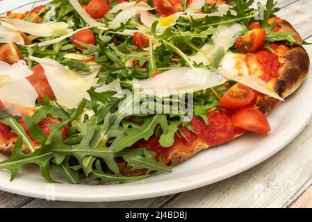 Dettaglio di una deliziosa pizza, con scaglie di parmigiano, rucola in abbondanza, salsa di pomodoro e pomodori ciliegini tritati con olio d'oliva spagnolo Foto Stock