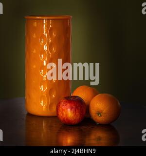 Foto di natura morta scura e atmosferica, fiasca vuota per fiori, arance e mele, realizzata con luce naturale. Foto Stock
