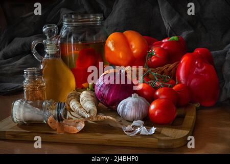 Foto di natura morta scura e atmosferica, verdure, pepe rosso, pepe giallo, olio d'oliva, radice di prezzemolo, spremitore di sale, spezie, a luce naturale. Foto Stock