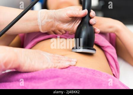 Cosmetologo qualificato che esegue la procedura ecografica cavitazione del corpo per il cliente femminile in clinica Foto Stock