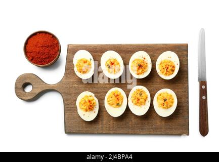 Tagliere con gustose uova ripiene, paprika e coltello su sfondo bianco. Festa di Pasqua Foto Stock