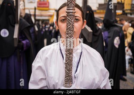 Siviglia, Spagna. 13th Apr 2022. Una ragazza cristiana ha visto portare una croce d'argento attraverso le strade di Siviglia, mentre prende parte ad una processione durante il mercoledì Santo per celebrare le celebrazioni della settimana Santa. La Confraternita di San Bernardo porta in strada la processione di el Cristo de la Salud e la Virgen del Refugio dopo due anni senza celebrare la settimana Santa a causa delle restrizioni della pandemia del Covid-19. Credit: SOPA Images Limited/Alamy Live News Foto Stock