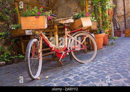 Una classica bicicletta rossa è decorata con tappi e casse di vino su una strada lastricata di Orvieto, Italia Foto Stock