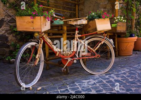 Una classica bicicletta rossa è decorata con tappi e casse di vino su una strada lastricata di Orvieto, Italia Foto Stock