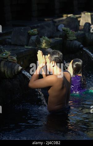 Un uomo che prega dopo aver fatto il bagno nella piscina del tempio Tirta Empul a Tampaksiring, Gianyar, Bali, Indonesia. Foto Stock