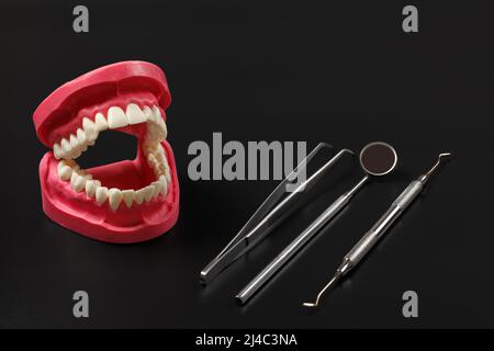 Set di strumenti metallici per il trattamento dentale con disposizione della mandibola umana. Pinzette, uno specchio della bocca e uno strumento di restauro dentale sul blac Foto Stock