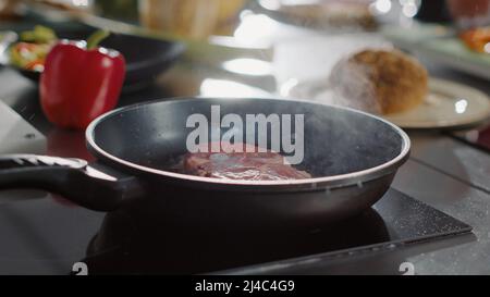 Carne di manzo cotta con olio di girasole biologico in padella su cucina, cottura a vapore e tostatura. Deliziosa bistecca fritta affumicata, preparazioni per piatti professionali. Primo piano. Scatto portatile. Foto Stock