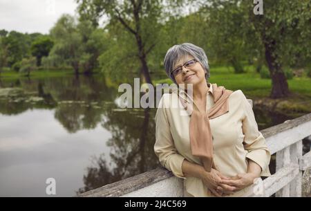Sorridente anziana donna dai capelli grigi rilassarsi vicino al lago Foto Stock