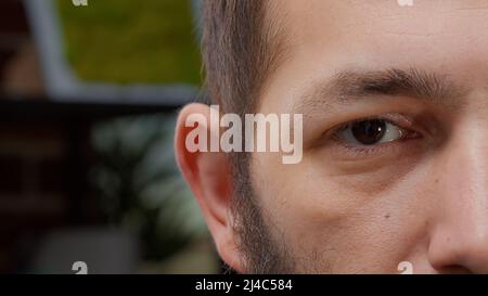 Foto macro dell'uomo che mostra un occhio e mezzo volto sulla fotocamera, mostrando espressioni facciali felici. Uomo che si sente sicuro e sorridente, con occhi marroni e denti bianchi. Primo piano. Foto Stock