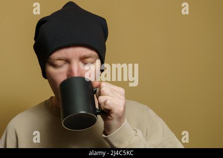 Ritratto di un uomo in un cappello nero con una tazza nera, primo piano Foto Stock