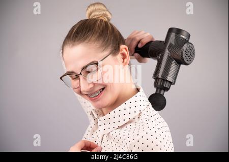 Donna sorridente con bretelle usa una pistola massaggiatore per la schiena. Foto Stock