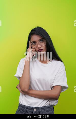 Ragazza indiana asiatica premurosa giovane in cerca di soluzione, pensando attentamente guardando via. Sfondo verde isolato. Foto Stock