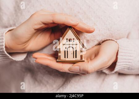 Donna che tiene una casa di legno con le mani con il sole su uno sfondo rosa chiaro. Dolce casa, assicurazione Foto Stock