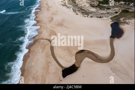 Vista con droni ad alto angolo di un'ampia e infinita spiaggia di sabbia dorata con un fiume che scorre verso l'oceano Foto Stock