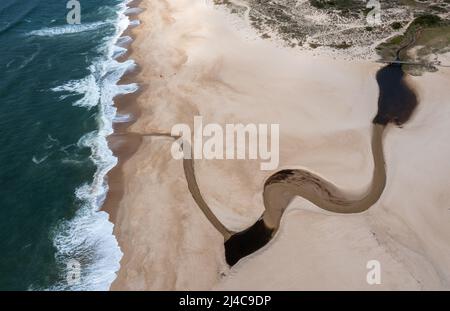 Vista con droni ad alto angolo di un'ampia e infinita spiaggia di sabbia dorata con un fiume che scorre verso l'oceano Foto Stock