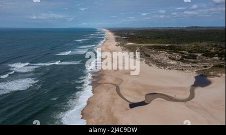 Vista con droni ad alto angolo di un'ampia e infinita spiaggia di sabbia dorata con un fiume che scorre verso l'oceano Foto Stock