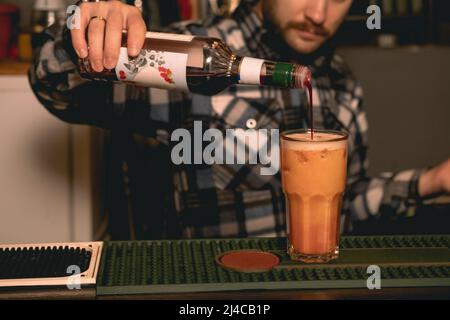 Barista preparare Tequila Sunrise cocktail, aggiungendo sciroppo di melograno in bicchiere con bevanda Foto Stock