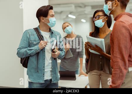 Gli studenti indossano maschere protettive e parlano tra loro Foto Stock