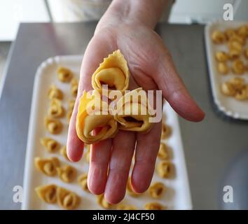 La cuoca italiana ha in mano tre tortellini crudi. Foto Stock