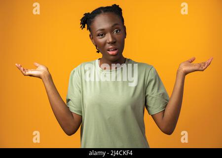 Puzzled e la giovane donna africana clueless con le armi fuori in studio giallo Foto Stock