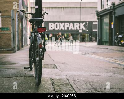 Shoreditch, Londra, Regno Unito - 14 aprile 2016: Una bicicletta stazionaria, con il centro commerciale Boxpark visibile sullo sfondo. Foto Stock