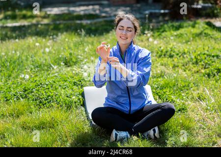 Primavera e felicità. Una giovane donna siede sul prato del suo cortile e tiene un dente di leone con un sorriso. Foto Stock