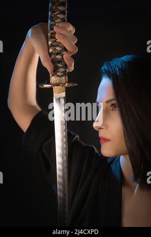 Primo piano ritratto di una giovane donna guerriera con un katana, guardando una lama affilata. Foto Stock