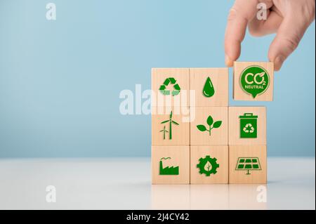 Concetto di zero netto e neutro di carbonio. Mettere i cubetti di legno con l'icona verde netto zero. Mettere a mano i cubi di legno con l'icona verde netto zero e l'icona verde su blu Foto Stock