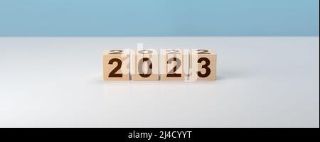 Blocchi di legno con 2022 2023 numero su sfondo grigio. Nuovo anno concetto. Cubo di legno con flip sopra blocco 2022 a 2023 parola. Gestione aziendale, Ins Foto Stock