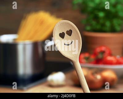 cucchiaio da cucina in legno con cuore sorridente davanti alla pentola con spaghetti e altri ingredienti