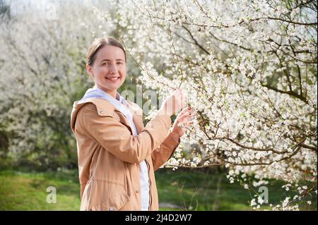 Donna allergica che soffre di allergia stagionale in primavera, posando in giardino fiorito in primavera. Ritratto di donna felice sorridente dopo il trattamento. Concetto di allergia primaverile Foto Stock