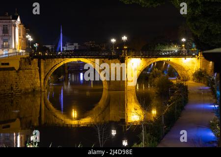 Scena stradale durante la serata con ponte vecchio illuminato che attraversa il fiume Segura in Murcia in Spagna Foto Stock