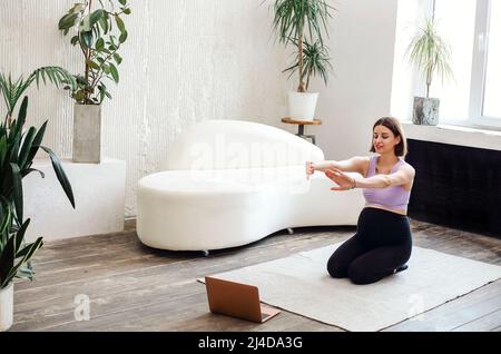 Donna incinta bruna felice con computer portatile che fa yoga a casa. Sport, fitness e concetto di persone Foto Stock