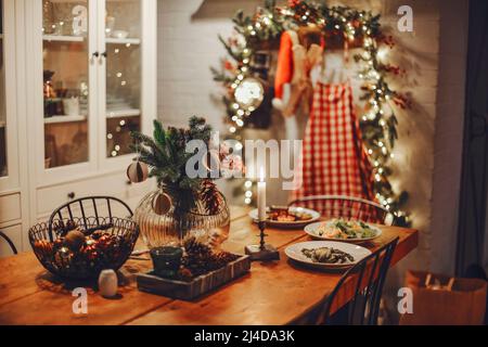 Festa inverno accogliente cucina interna con ghirlande, decorazioni e regali. Cena di Natale al tavolo decorato con piatti deliziosi Foto Stock