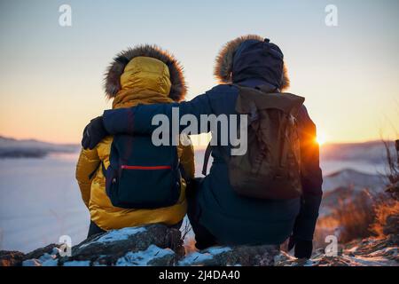 Coppia romantica di turisti vestito di abbigliamento sportivo invernale caldo con zaini turistici seduti nelle montagne innevate in un incredibile tramonto. Ogoi isla Foto Stock