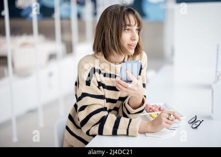 Giovane donna che usa il telefono mentre si siede al ristorante Foto Stock