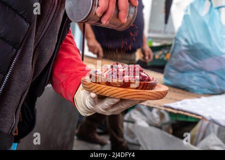 Mano di un uomo che versa la paprika su una porzione di Pulpo a feira, una ricetta popolare per il polpo in Galizia. Spagna Foto Stock