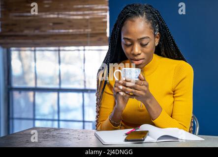 Giovane africano studente americano con maglietta gialla seduti al bancone cucina isola la scrittura in un notebook. Alla moda stile di vita etnica dell'immagine. Foto Stock