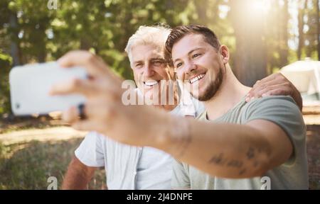 Sorridi. Scatto corto di un bel giovane uomo e suo padre che prende selfie mentre si accampano nei boschi. Foto Stock