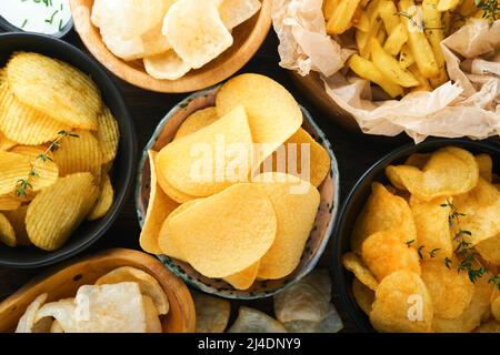 Cibo o spuntini malsani. Tutti i classici spuntini di patate con arachidi, anelli di popcorn e cipolle e pretzel salati in piatti da ciotola su vecchio sfondo di legno. Foto Stock