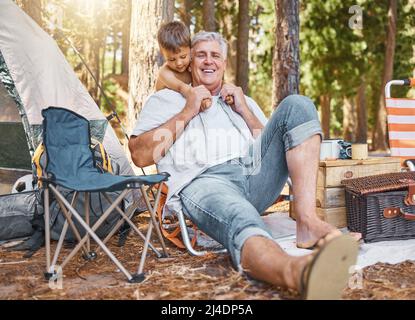 Campeggio con nonno. Scatto a tutta lunghezza di un bell'uomo maturo e di suo nipote seduto al loro campeggio nei boschi. Foto Stock